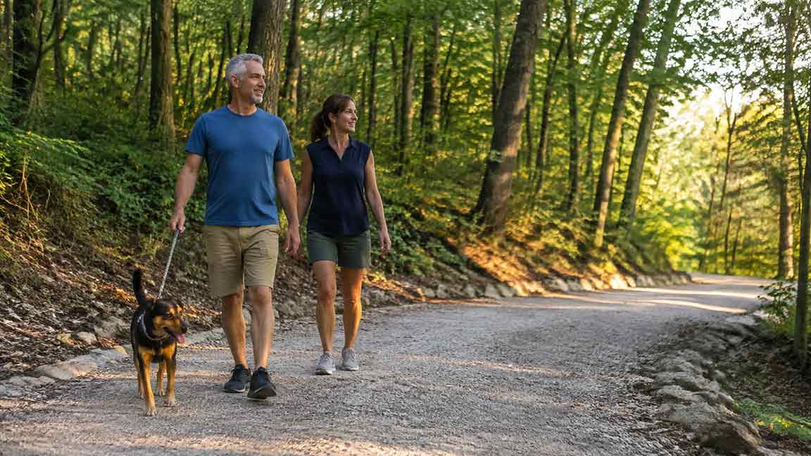 Couple with an adult who suffers from chronic pain walking a dog on a trail in Northwest Arkansas to celebrate Pain Awareness Month.