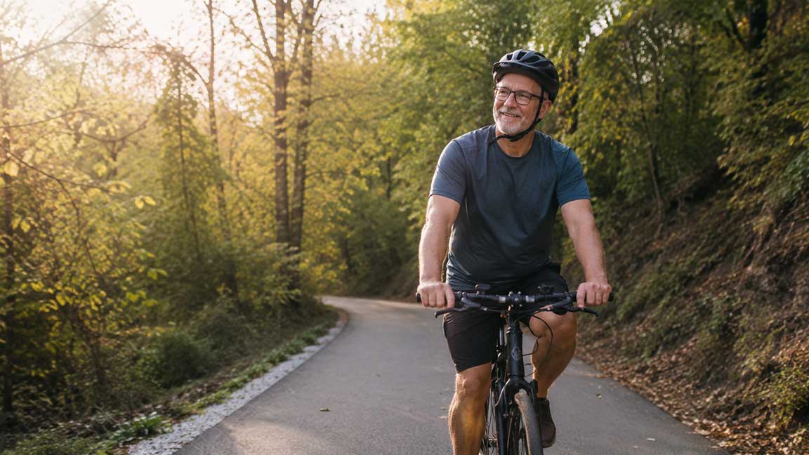 : Older man riding a bicycle along a wooded trail in Northwest Arkansas.
