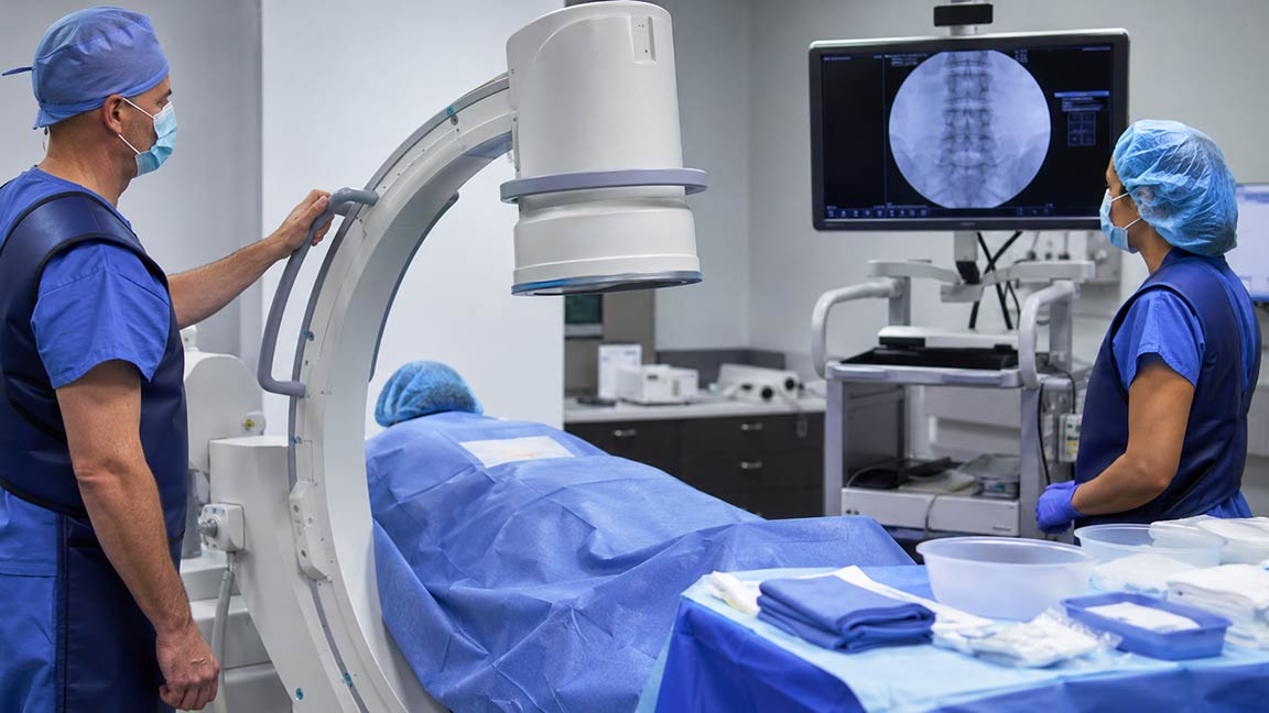 Medical team prepares C-arm fluoroscopy equipment for an image-guided pain procedure.